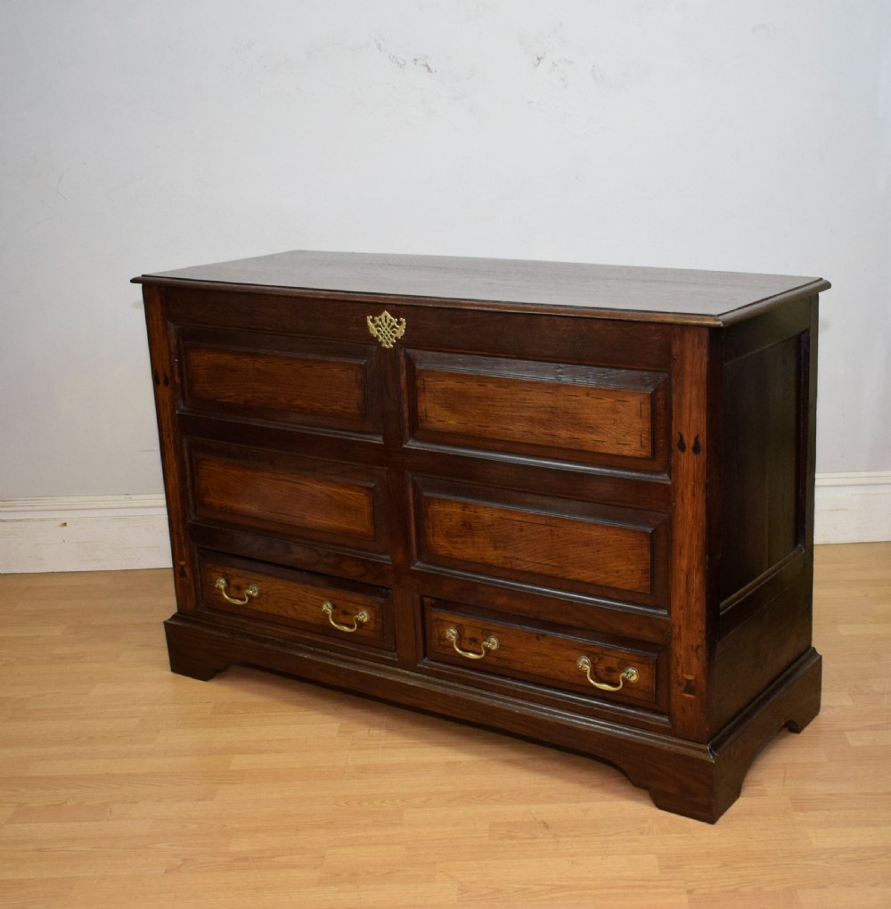 A Georgian dark oak Lancashire mule chest featuring a hinged top lid, panelled front sections with inlays, brass swan-neck handles, and bracket feet. View II