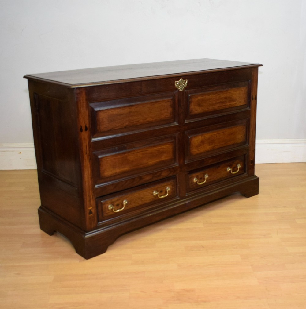 A Georgian dark oak Lancashire mule chest featuring a hinged top lid, panelled front sections with inlays, brass swan-neck handles, and bracket feet. View V