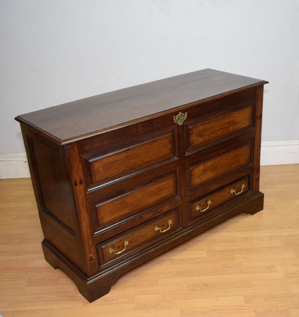 A Georgian dark oak Lancashire mule chest featuring a hinged top lid, panelled front sections with inlays, brass swan-neck handles, and bracket feet. View VI