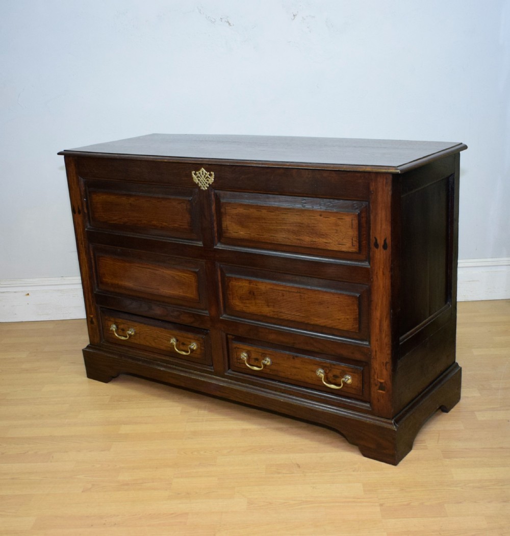 A Georgian dark oak Lancashire mule chest featuring a hinged top lid, panelled front sections with inlays, brass swan-neck handles, and bracket feet. View XV