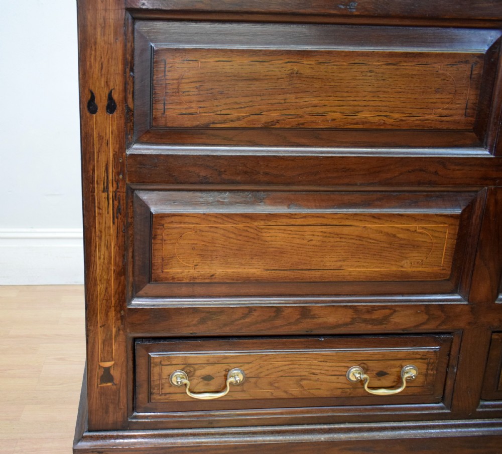 A Georgian dark oak Lancashire mule chest featuring a hinged top lid, panelled front sections with inlays, brass swan-neck handles, and bracket feet. View XXI