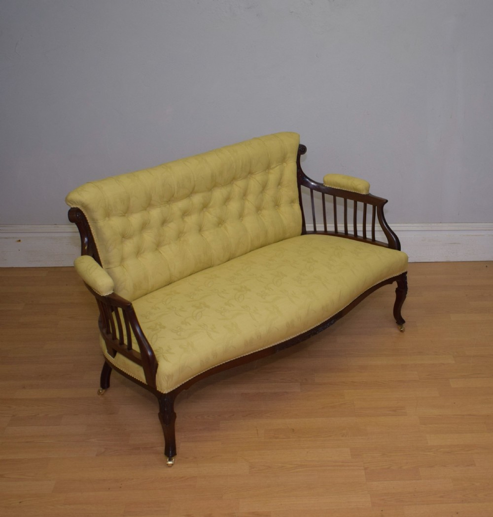 A Victorian mahogany settee featuring yellow tufted upholstery, open spindled arms, carved legs, and brass castors. View II