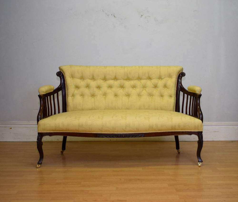 A Victorian mahogany settee featuring yellow tufted upholstery, open spindled arms, carved legs, and brass castors. View III