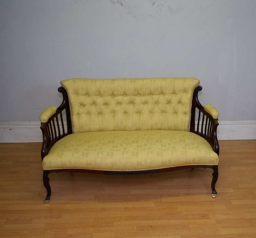 A Victorian mahogany settee featuring yellow tufted upholstery, open spindled arms, carved legs, and brass castors. View V