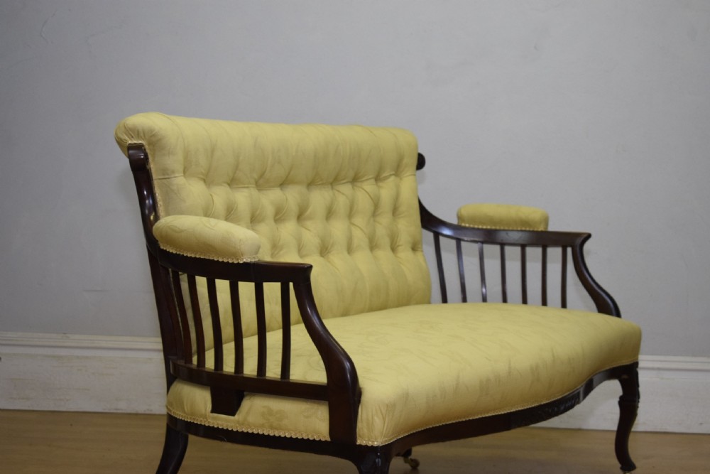 A Victorian mahogany settee featuring yellow tufted upholstery, open spindled arms, carved legs, and brass castors. View XI