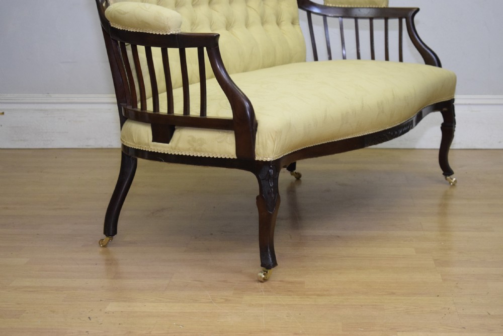 A Victorian mahogany settee featuring yellow tufted upholstery, open spindled arms, carved legs, and brass castors. View XII