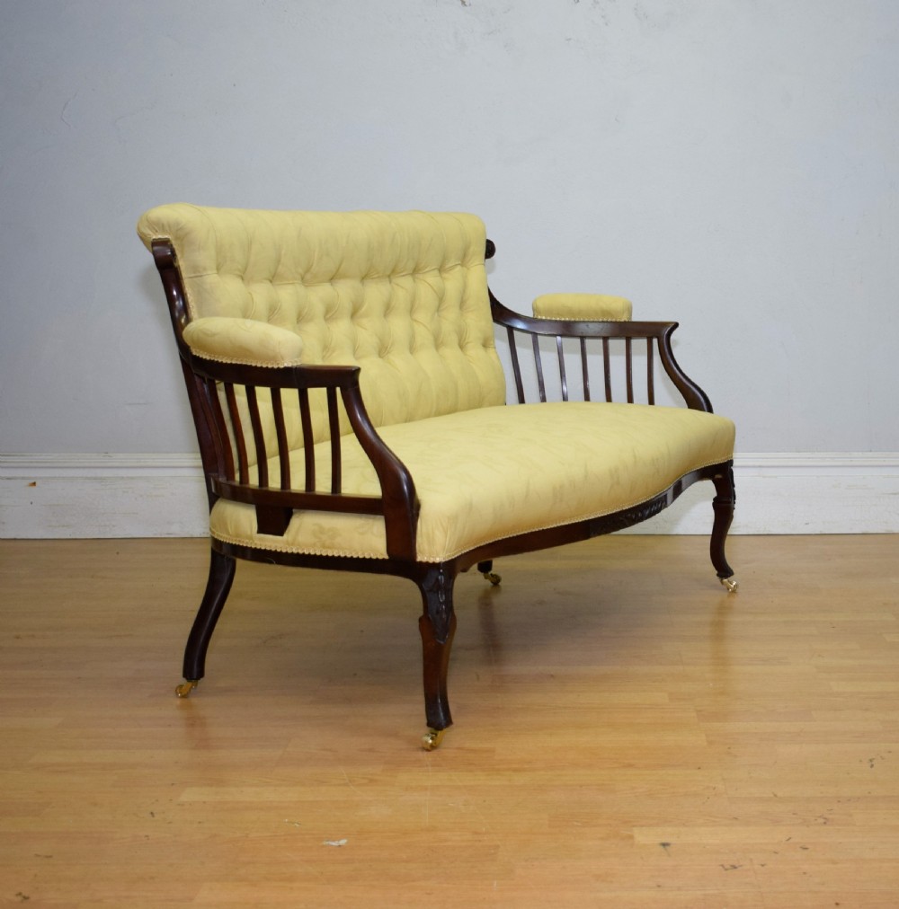 A Victorian mahogany settee featuring yellow tufted upholstery, open spindled arms, carved legs, and brass castors. View XIII