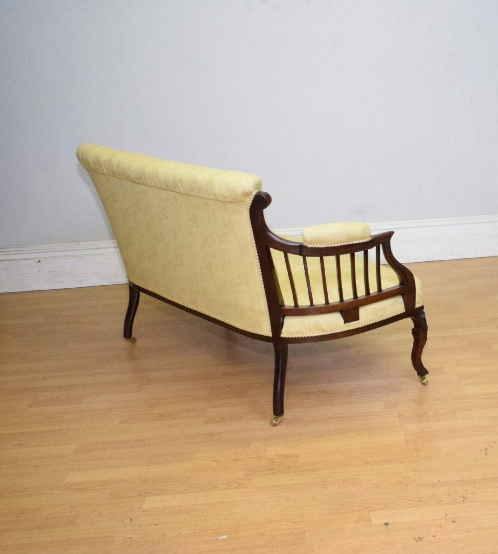 A Victorian mahogany settee featuring yellow tufted upholstery, open spindled arms, carved legs, and brass castors. View XIV