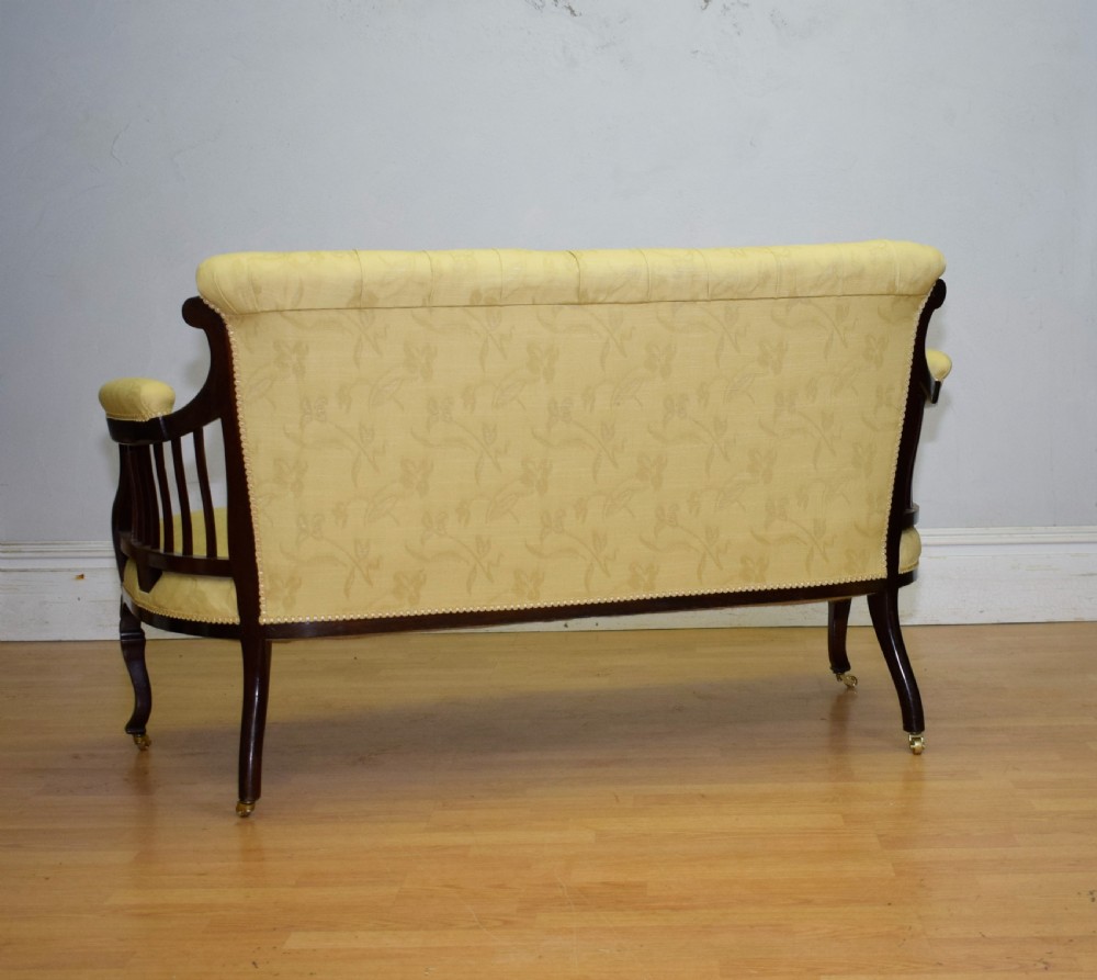 A Victorian mahogany settee featuring yellow tufted upholstery, open spindled arms, carved legs, and brass castors. View XV
