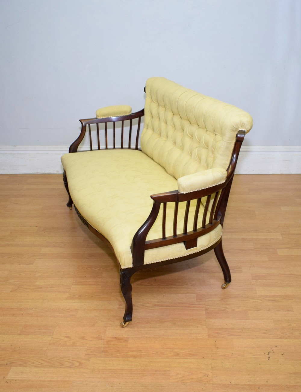 A Victorian mahogany settee featuring yellow tufted upholstery, open spindled arms, carved legs, and brass castors. View XVI