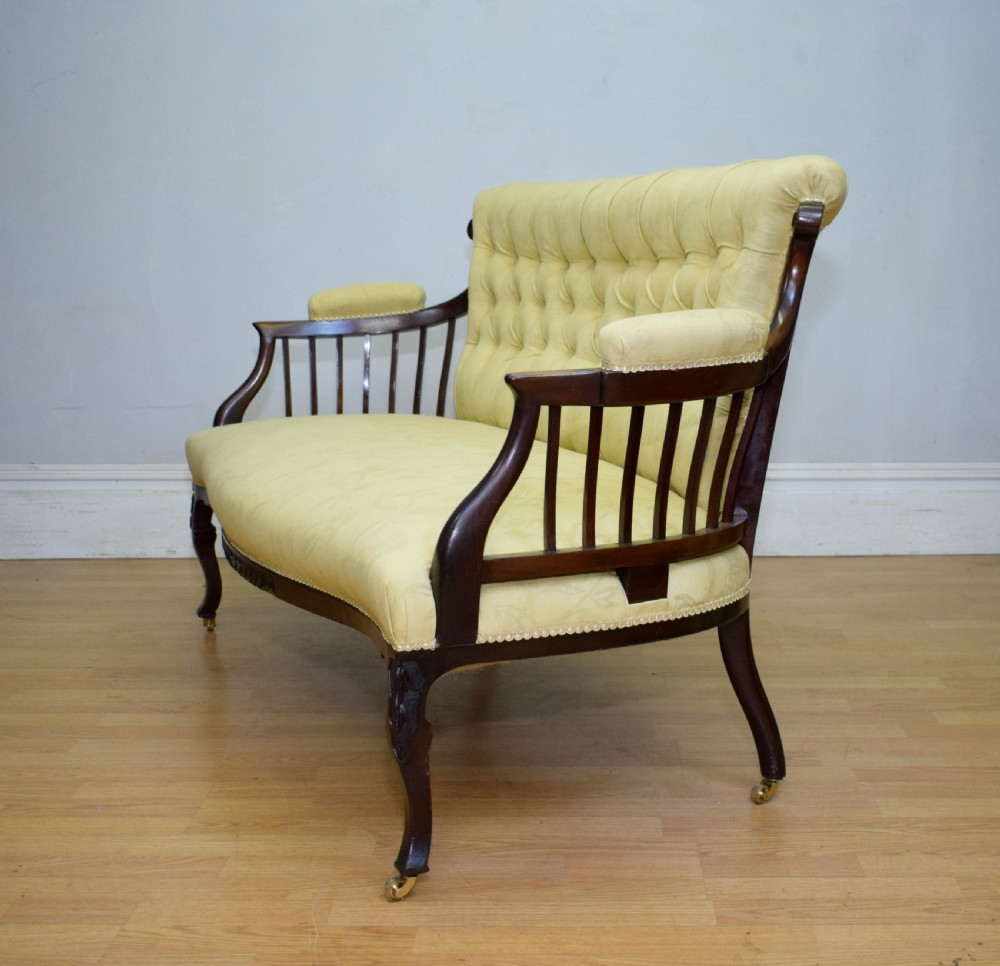 A Victorian mahogany settee featuring yellow tufted upholstery, open spindled arms, carved legs, and brass castors. View XVII