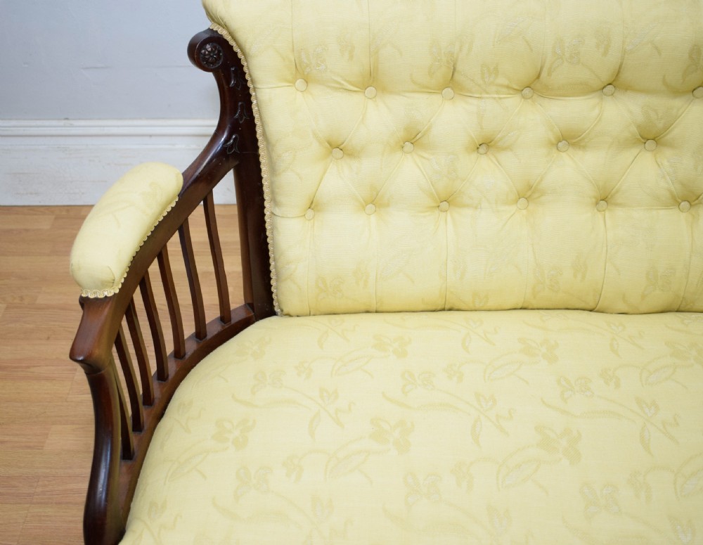 A Victorian mahogany settee featuring yellow tufted upholstery, open spindled arms, carved legs, and brass castors. View XIX