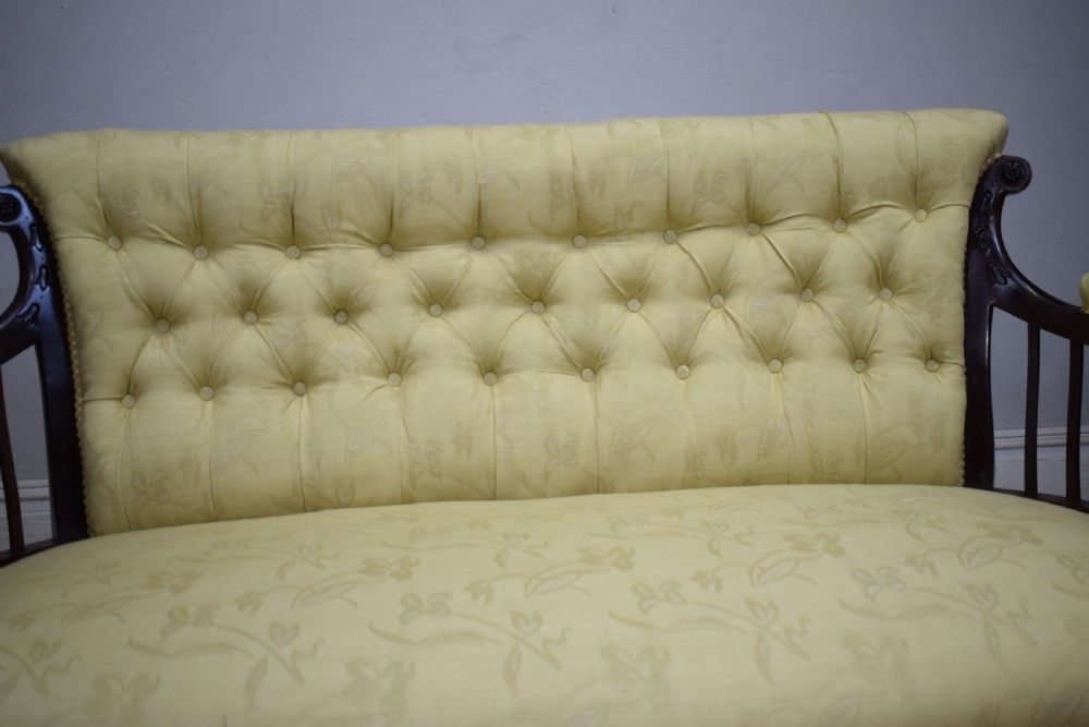 A Victorian mahogany settee featuring yellow tufted upholstery, open spindled arms, carved legs, and brass castors. View XX