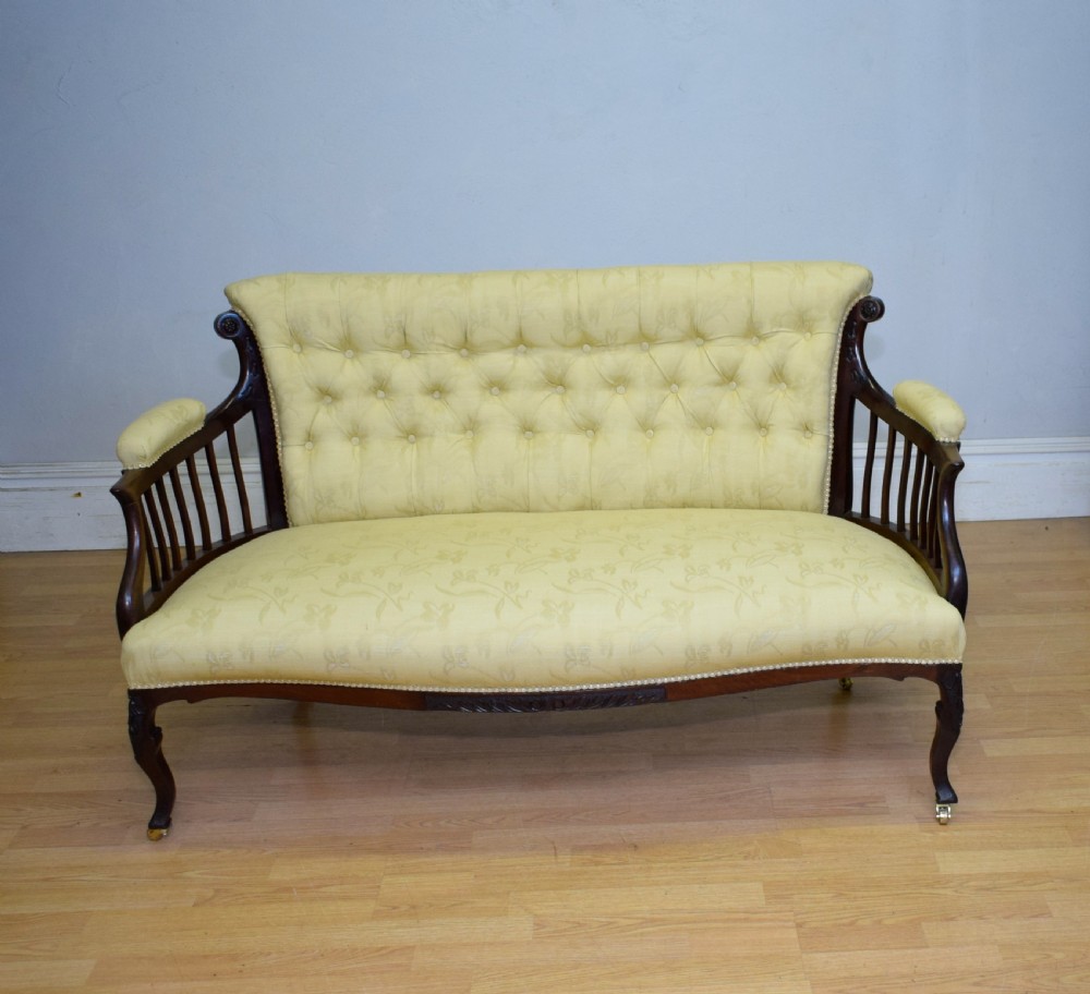 A Victorian mahogany settee featuring yellow tufted upholstery, open spindled arms, carved legs, and brass castors. View XXI