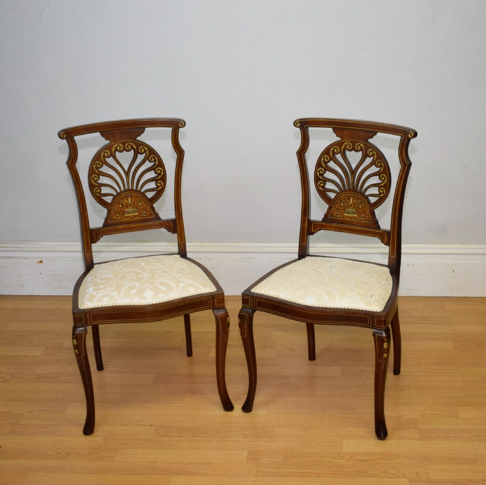 A pair of Victorian side chairs featuring dark mahogany frames with detailed marquetry inlays, fan-shaped pierced backrests, and cream upholstered seats.