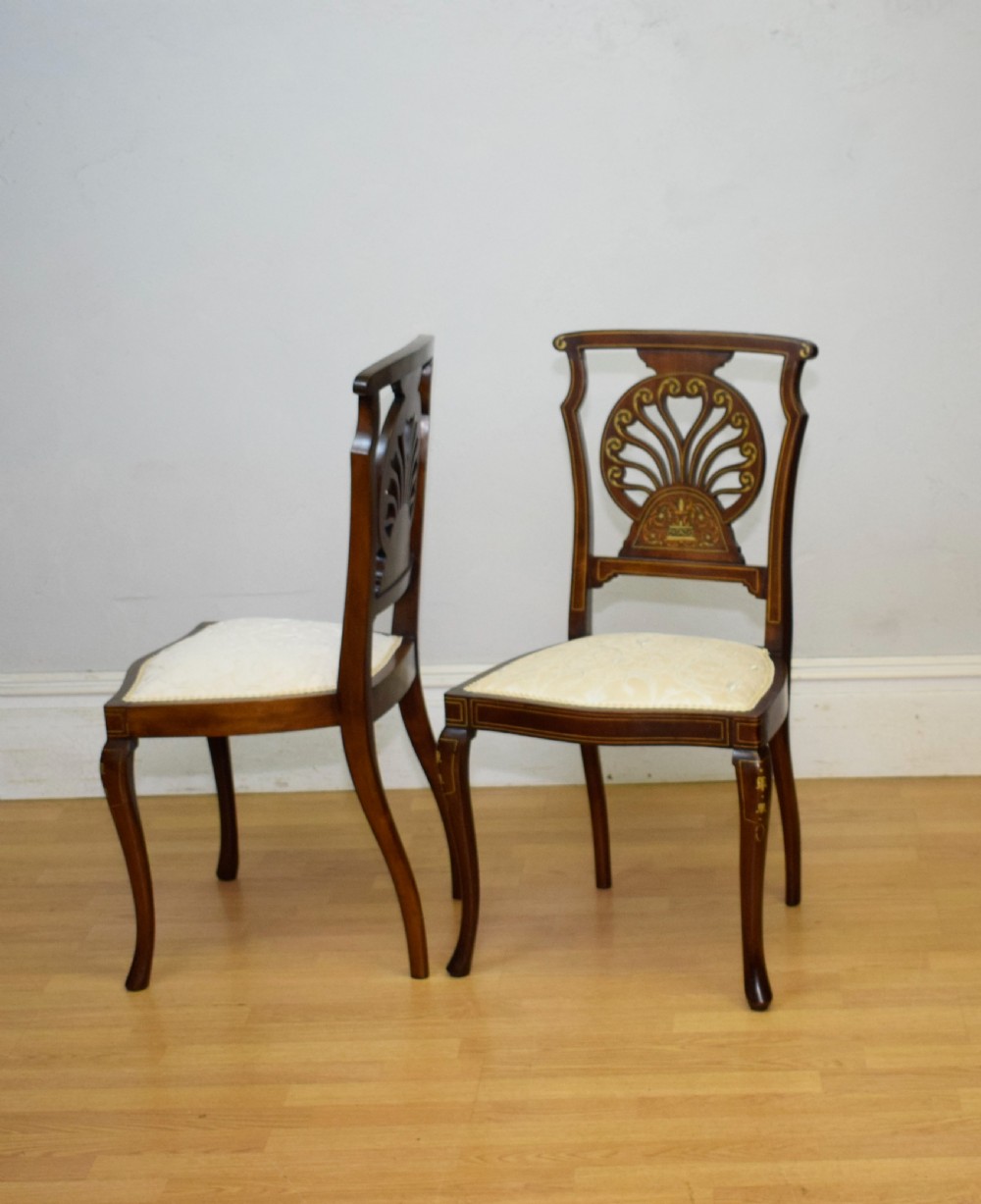 A pair of Victorian side chairs featuring dark mahogany frames with detailed marquetry inlays, fan-shaped pierced backrests, and cream upholstered seats. View XXI