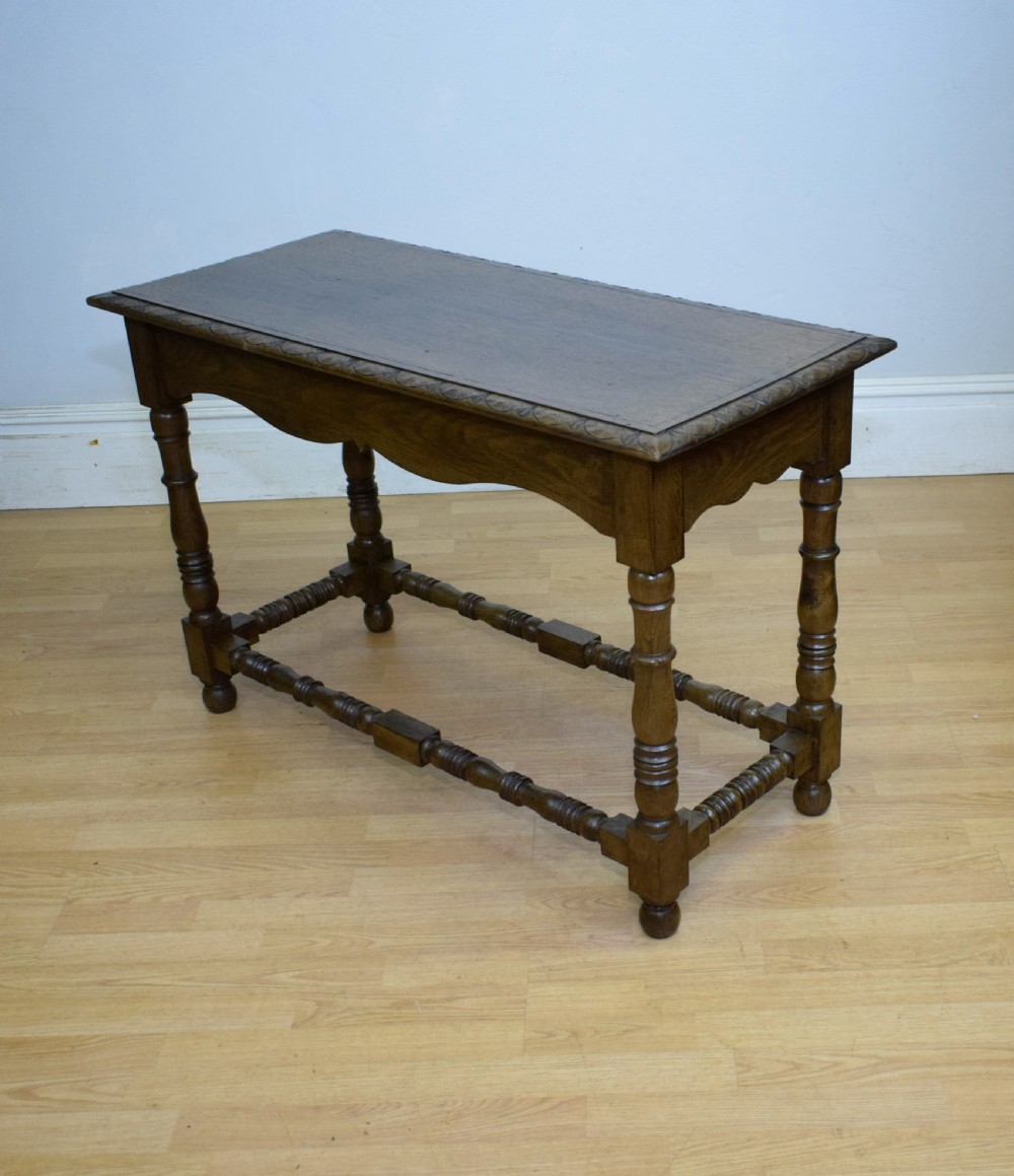 An early 20th-century oak console table featuring turned legs, a shaped apron, carved top edge, and low stretcher supports.