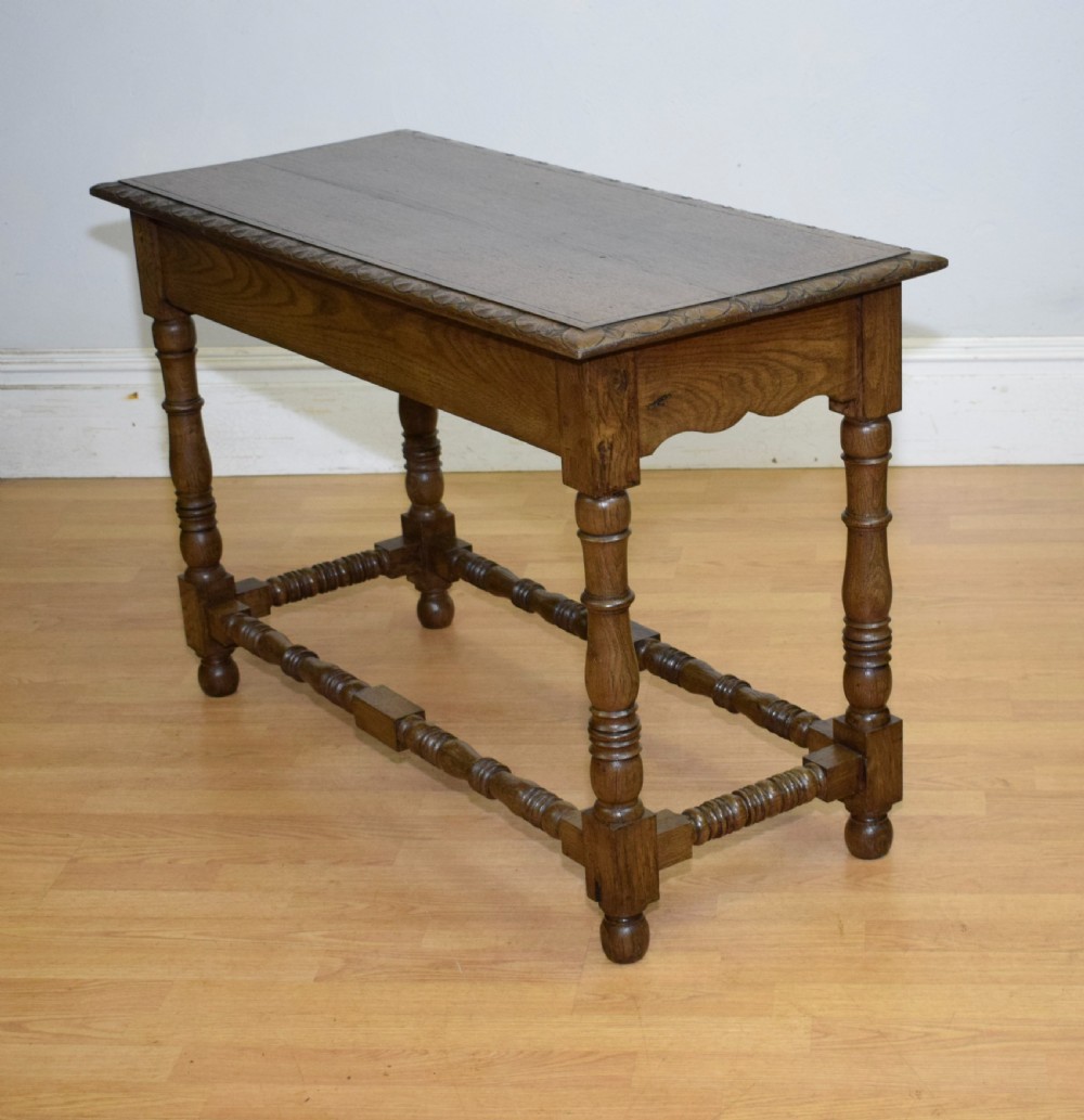 An early 20th-century oak console table featuring turned legs, a shaped apron, carved top edge, and low stretcher supports. View II