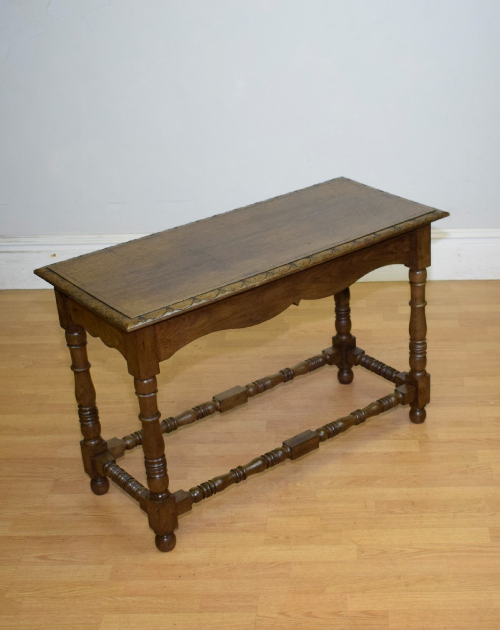 An early 20th-century oak console table featuring turned legs, a shaped apron, carved top edge, and low stretcher supports. View III