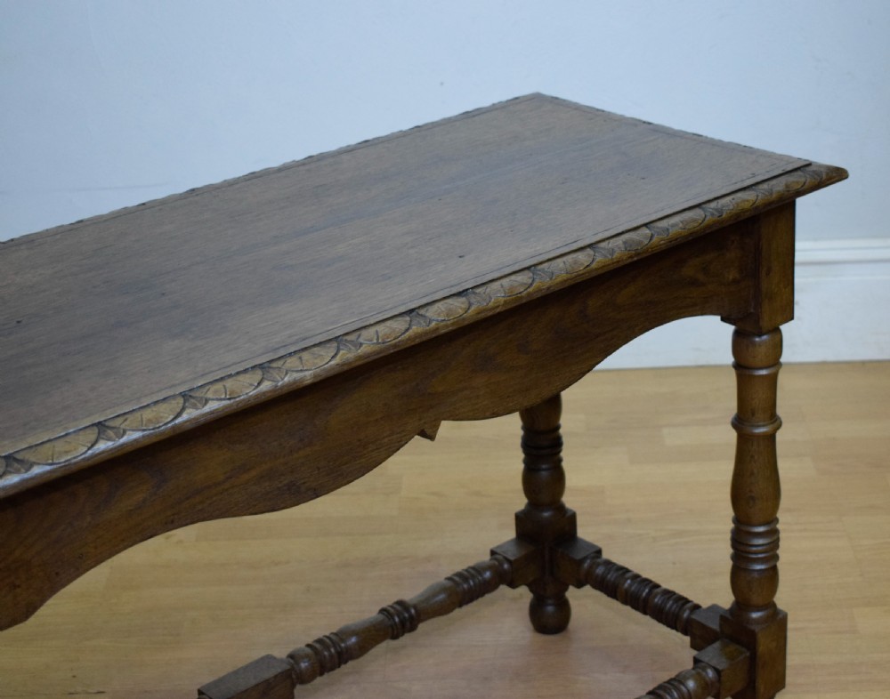An early 20th-century oak console table featuring turned legs, a shaped apron, carved top edge, and low stretcher supports. View VI