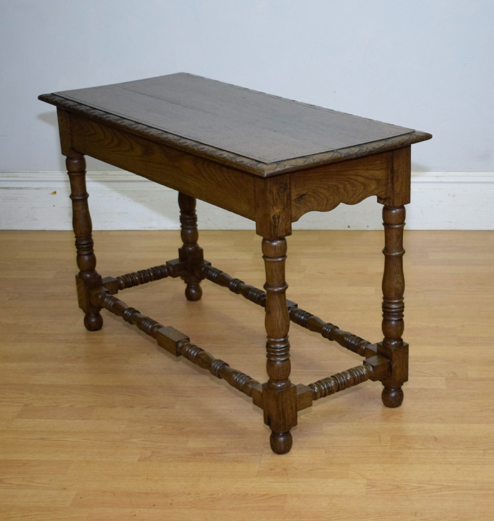 An early 20th-century oak console table featuring turned legs, a shaped apron, carved top edge, and low stretcher supports. View XXI