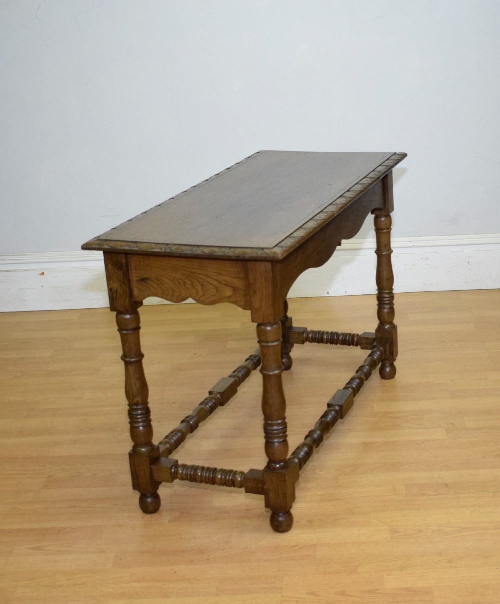 An early 20th-century oak console table featuring turned legs, a shaped apron, carved top edge, and low stretcher supports. View XXII