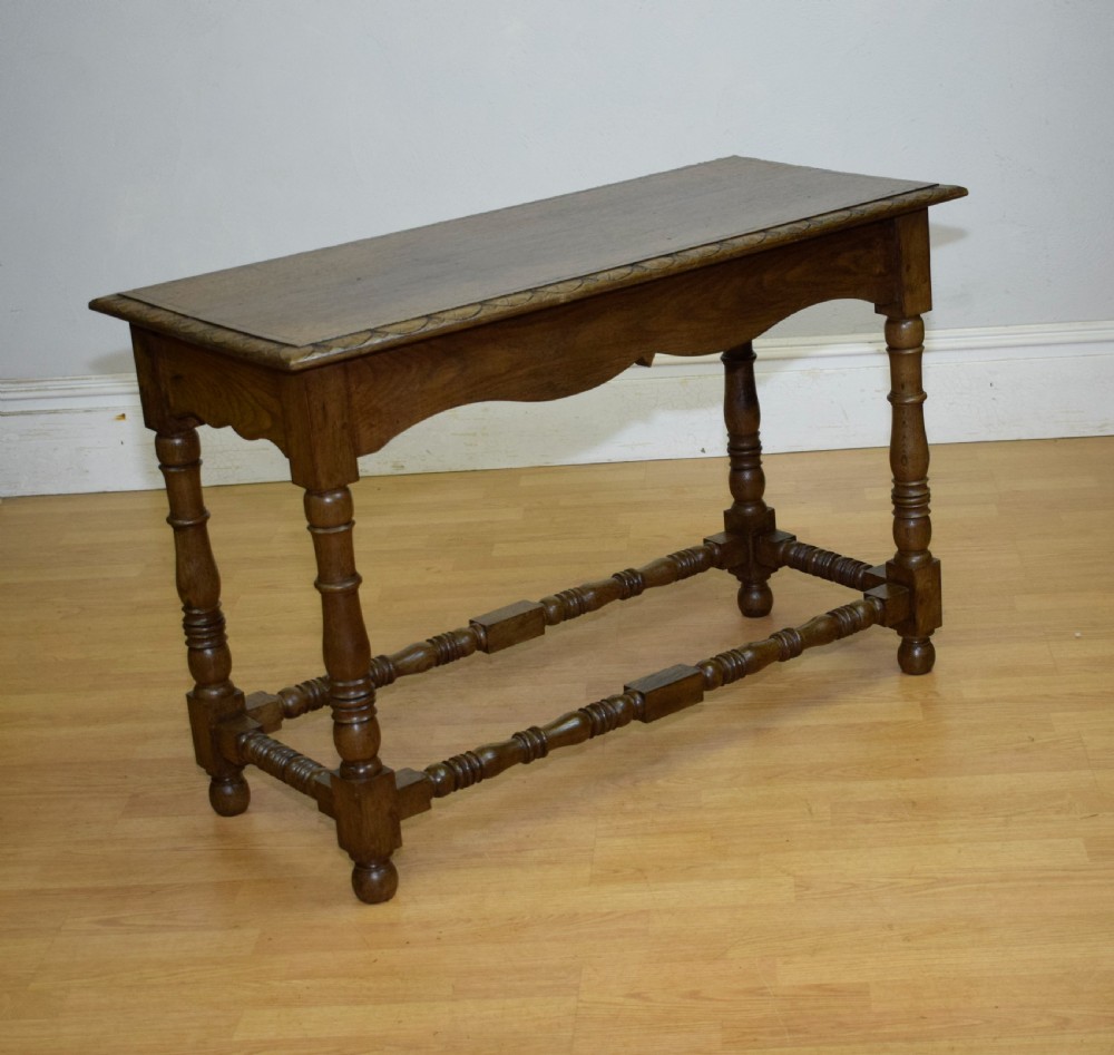 An early 20th-century oak console table featuring turned legs, a shaped apron, carved top edge, and low stretcher supports. View XXIII