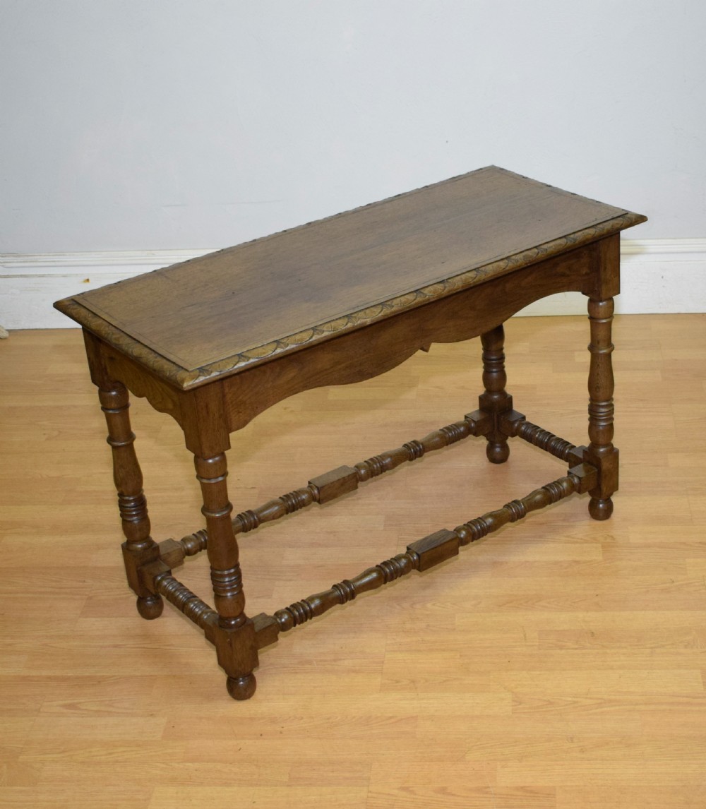 An early 20th-century oak console table featuring turned legs, a shaped apron, carved top edge, and low stretcher supports. View XXIV
