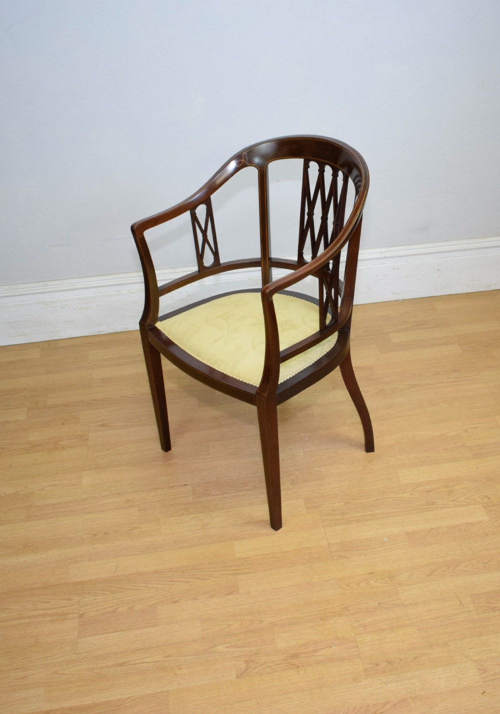 An Edwardian dark mahogany tub armchair featuring boxwood stringing inlay, pierced lattice back panels, and a yellow patterned upholstered seat. View II