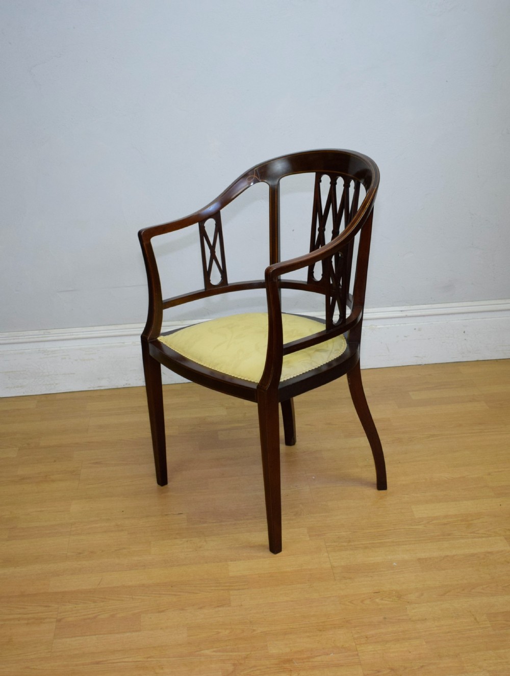 An Edwardian dark mahogany tub armchair featuring boxwood stringing inlay, pierced lattice back panels, and a yellow patterned upholstered seat. View IV