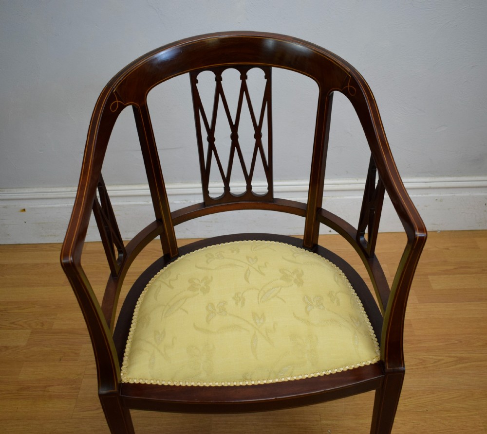 An Edwardian dark mahogany tub armchair featuring boxwood stringing inlay, pierced lattice back panels, and a yellow patterned upholstered seat. View XV