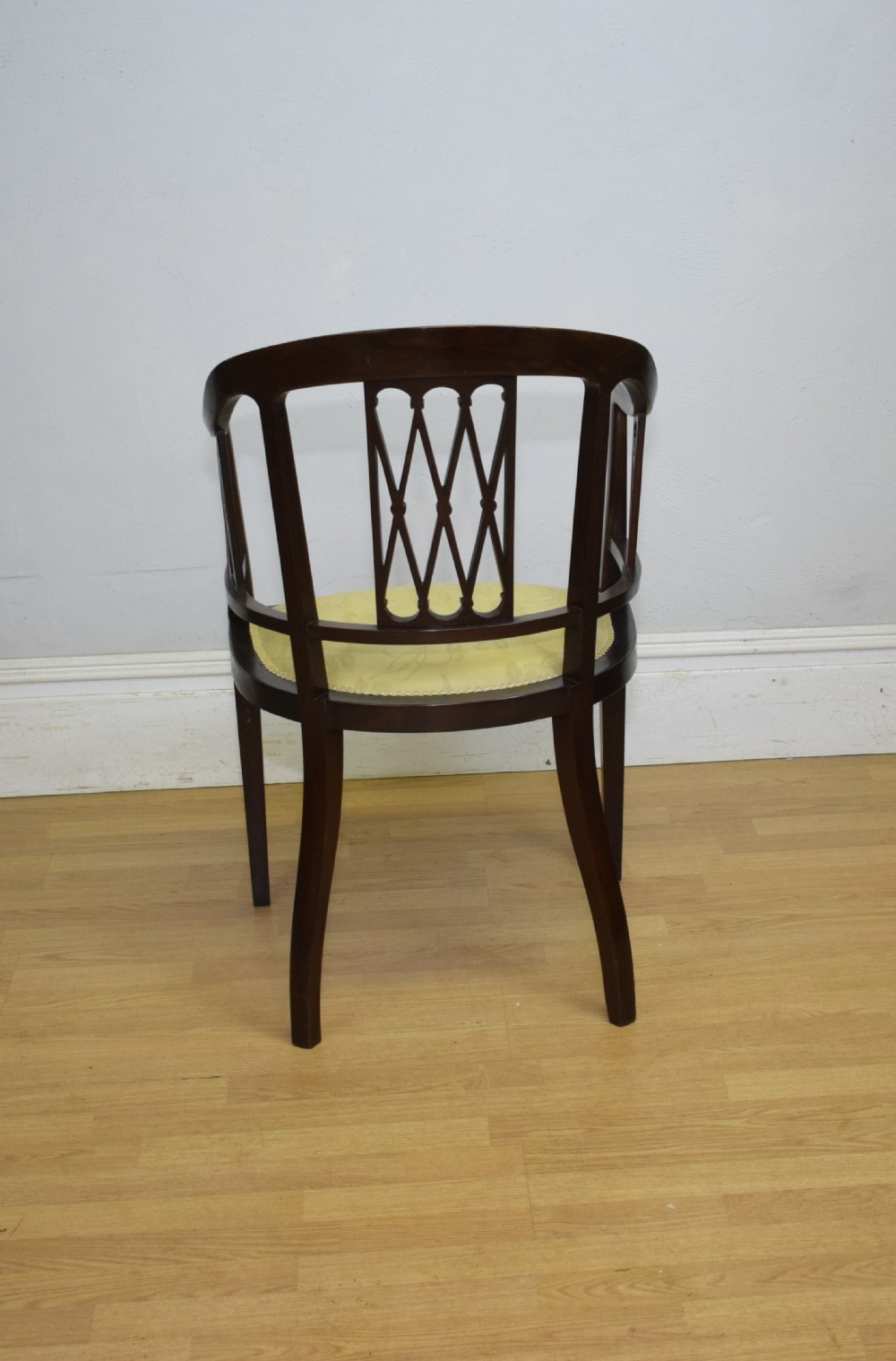 An Edwardian dark mahogany tub armchair featuring boxwood stringing inlay, pierced lattice back panels, and a yellow patterned upholstered seat. View XVII
