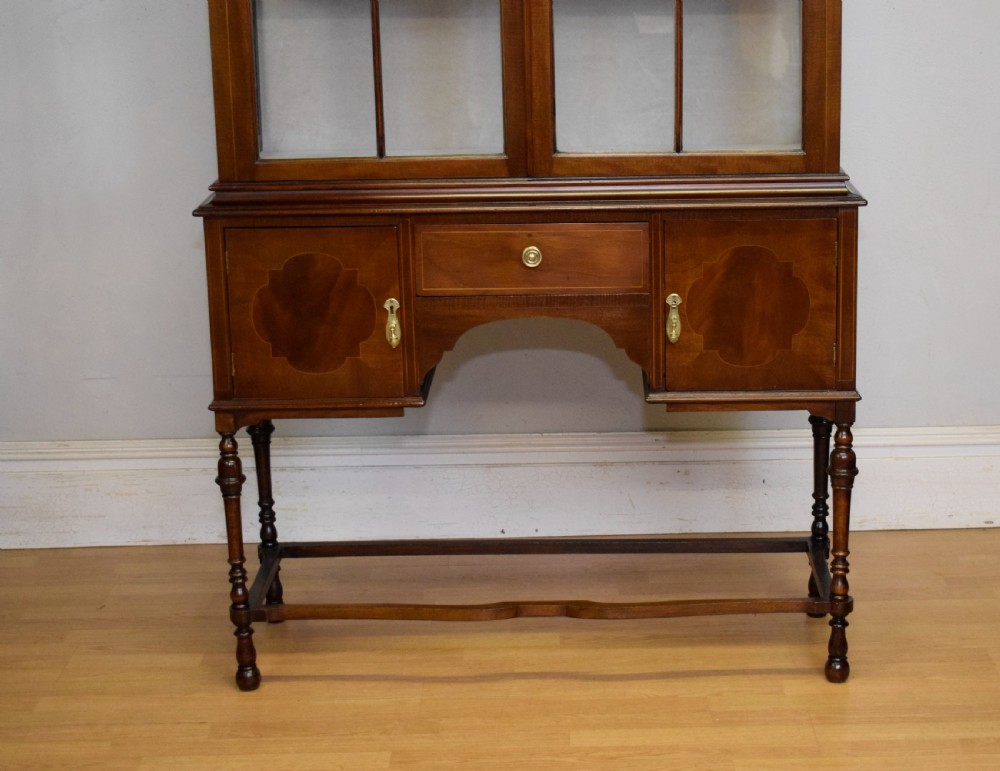 An early 20th-century mahogany display cabinet featuring double astragal glazed doors, an arched pediment top, lower cupboard section, and turned legs with stretchers. View V