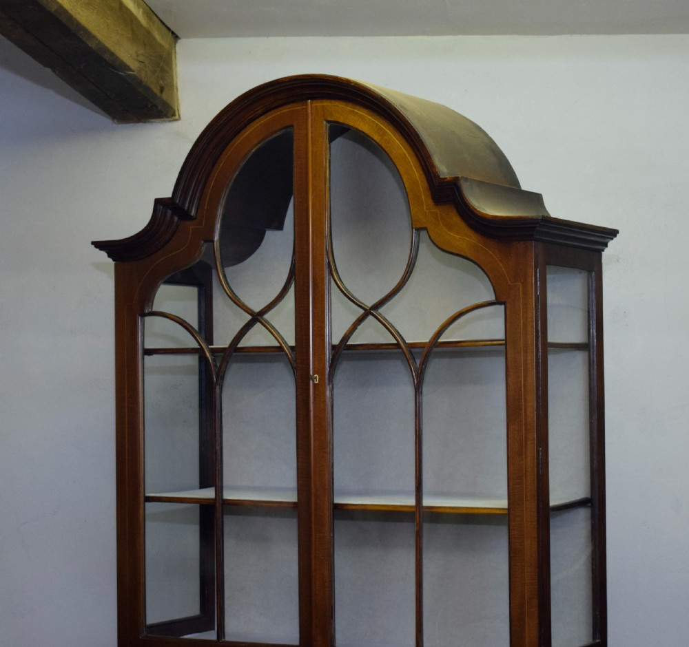 An early 20th-century mahogany display cabinet featuring double astragal glazed doors, an arched pediment top, lower cupboard section, and turned legs with stretchers. View XI
