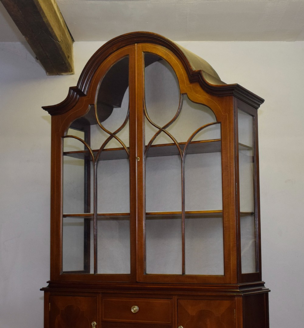 An early 20th-century mahogany display cabinet featuring double astragal glazed doors, an arched pediment top, lower cupboard section, and turned legs with stretchers. View XII