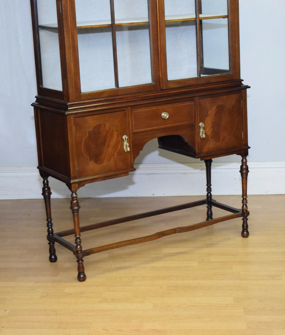 An early 20th-century mahogany display cabinet featuring double astragal glazed doors, an arched pediment top, lower cupboard section, and turned legs with stretchers. View XIV