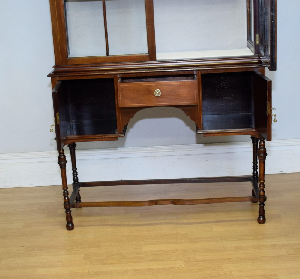 An early 20th-century mahogany display cabinet featuring double astragal glazed doors, an arched pediment top, lower cupboard section, and turned legs with stretchers. View XVIII