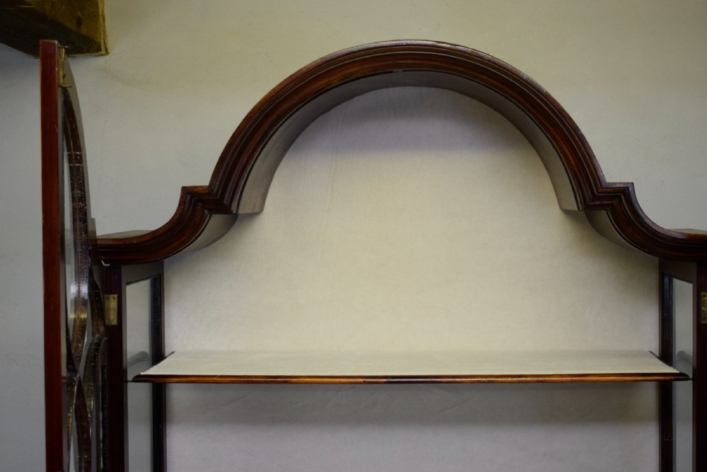 An early 20th-century mahogany display cabinet featuring double astragal glazed doors, an arched pediment top, lower cupboard section, and turned legs with stretchers. View XXI