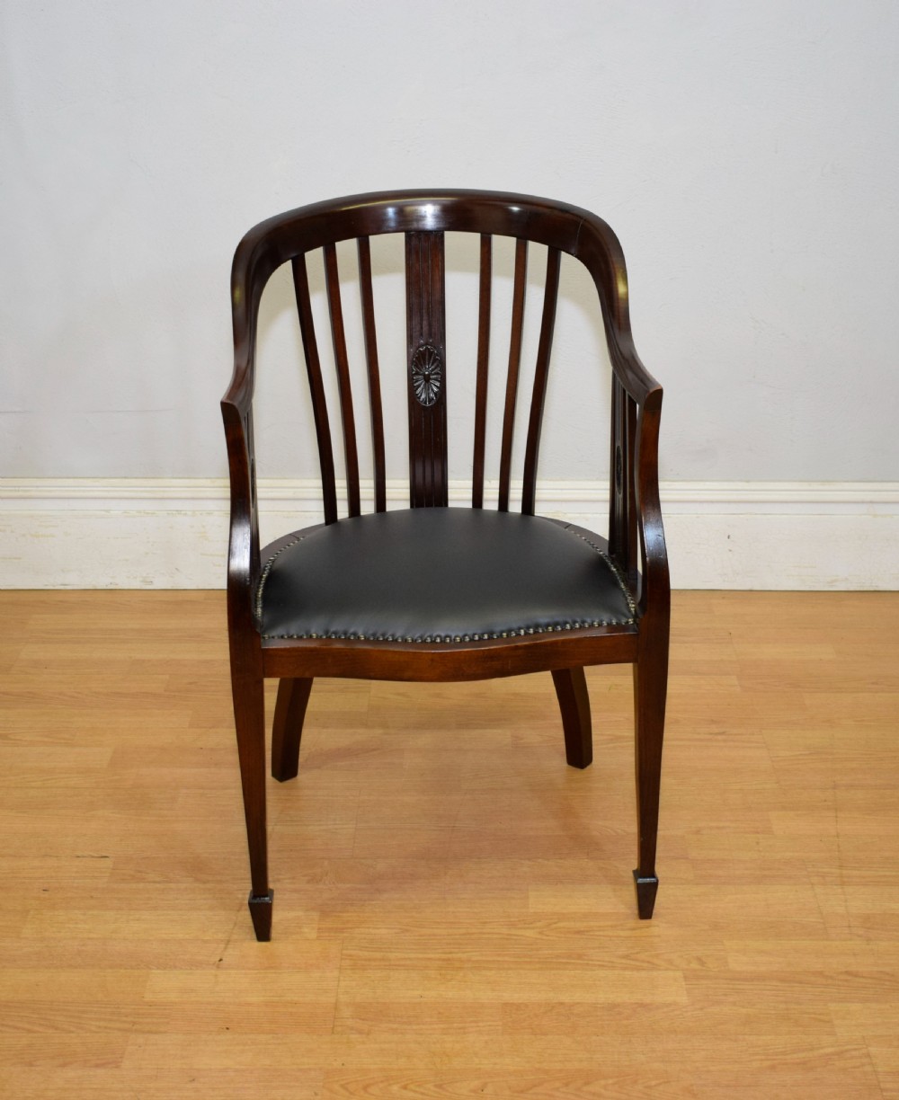A Victorian dark mahogany tub chair featuring a curved backrest with vertical splats, a central carved oval patera, and a black leather studded seat.