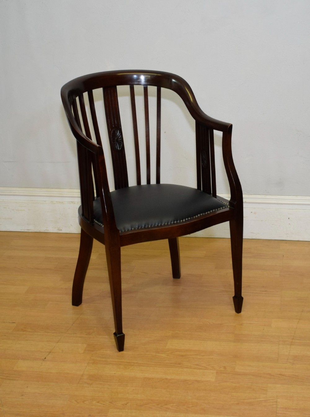 A Victorian dark mahogany tub chair featuring a curved backrest with vertical splats, a central carved oval patera, and a black leather studded seat. View VI