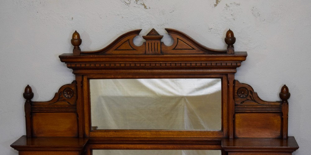 A Victorian carved oak overmantel mirror featuring turned side columns, small side display shelves, an arched pediment, and mirrored glass panels. View II