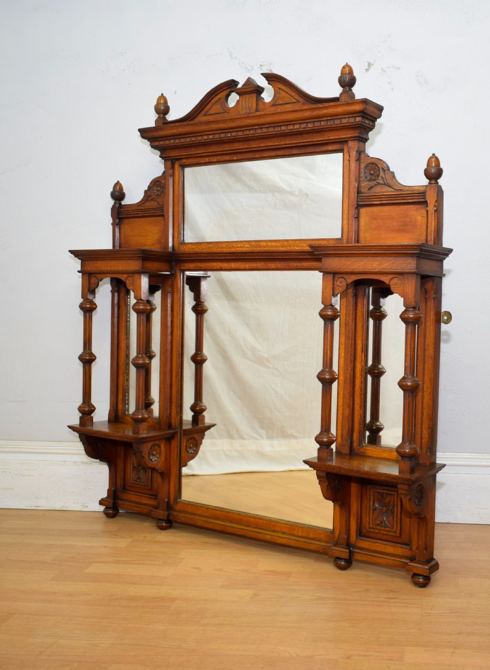 A Victorian carved oak overmantel mirror featuring turned side columns, small side display shelves, an arched pediment, and mirrored glass panels. View III