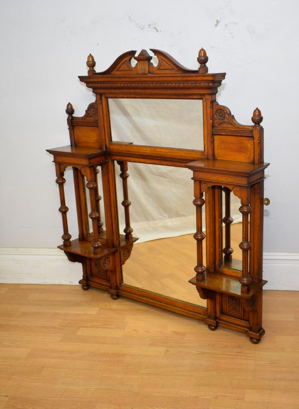 A Victorian carved oak overmantel mirror featuring turned side columns, small side display shelves, an arched pediment, and mirrored glass panels. View V