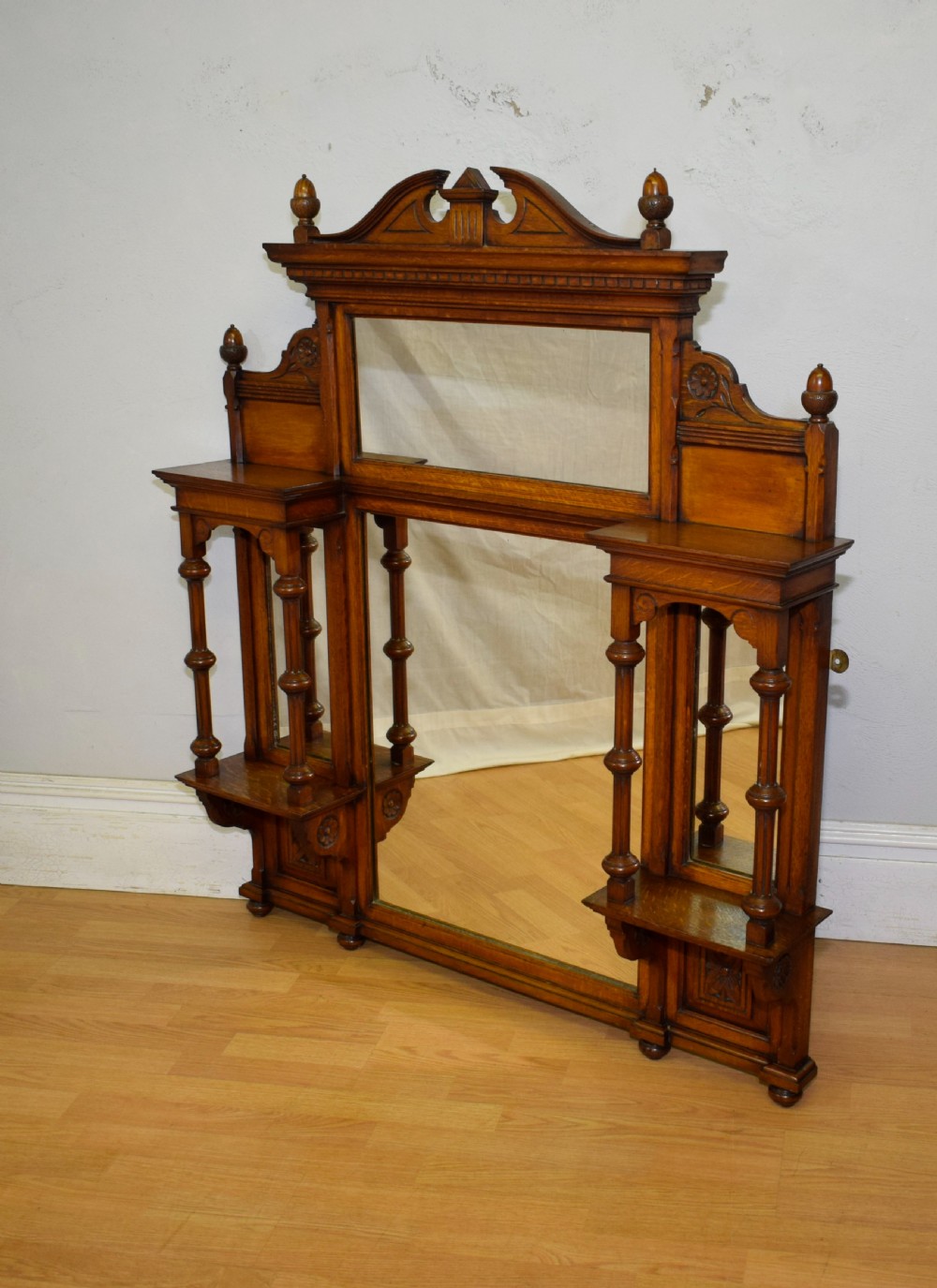 A Victorian carved oak overmantel mirror featuring turned side columns, small side display shelves, an arched pediment, and mirrored glass panels. View VI