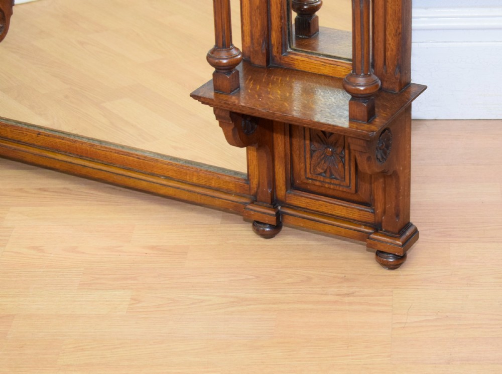 A Victorian carved oak overmantel mirror featuring turned side columns, small side display shelves, an arched pediment, and mirrored glass panels. View VII
