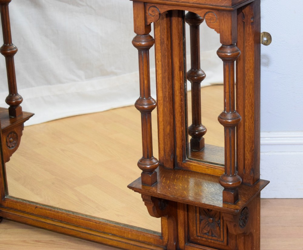 A Victorian carved oak overmantel mirror featuring turned side columns, small side display shelves, an arched pediment, and mirrored glass panels. View VIII