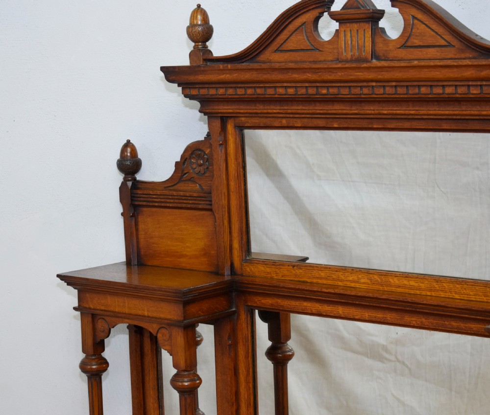 A Victorian carved oak overmantel mirror featuring turned side columns, small side display shelves, an arched pediment, and mirrored glass panels. View IX