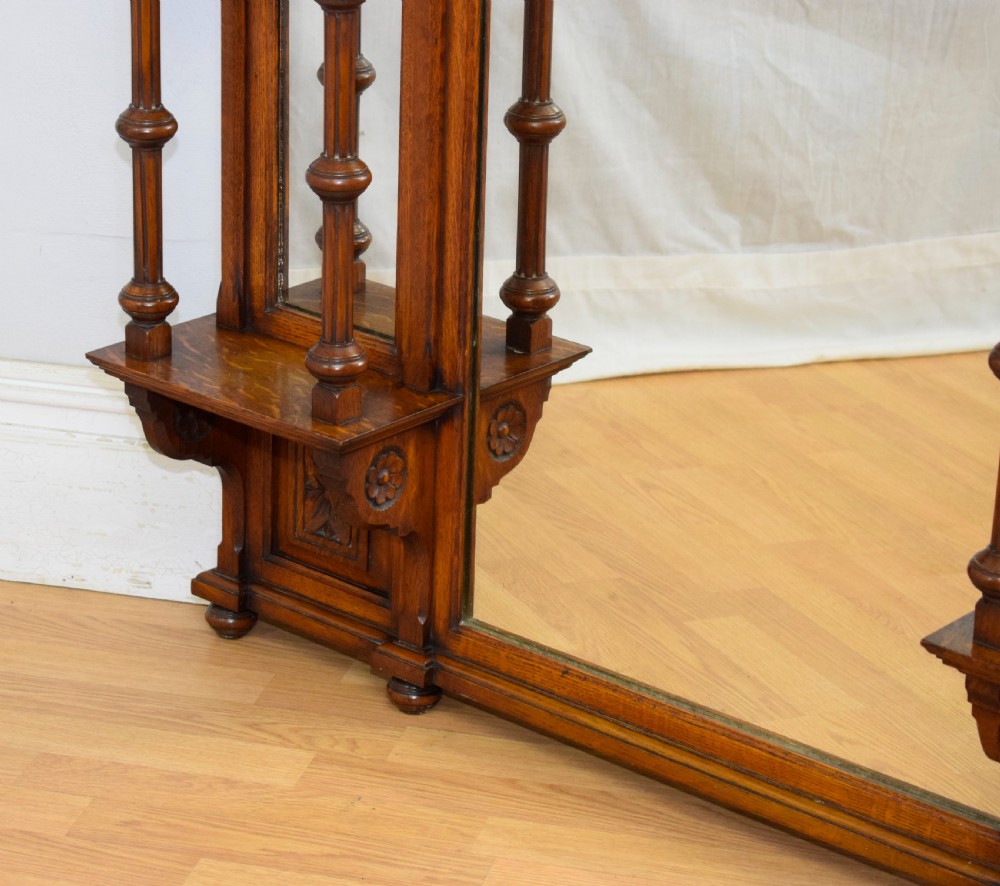 A Victorian carved oak overmantel mirror featuring turned side columns, small side display shelves, an arched pediment, and mirrored glass panels. View XI