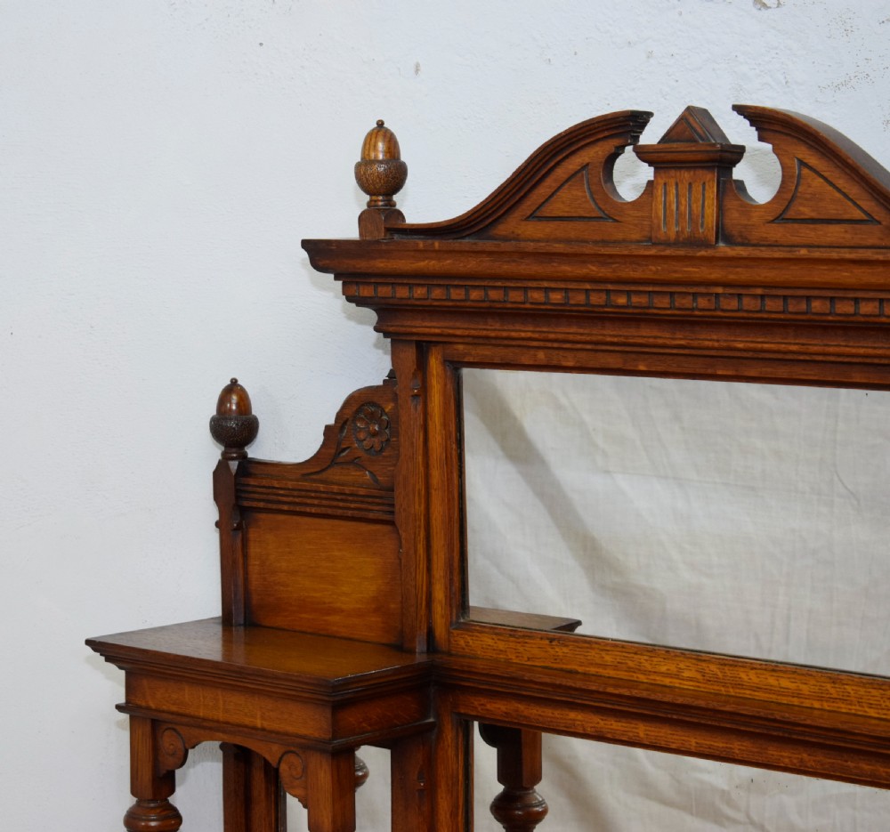 A Victorian carved oak overmantel mirror featuring turned side columns, small side display shelves, an arched pediment, and mirrored glass panels. View XII
