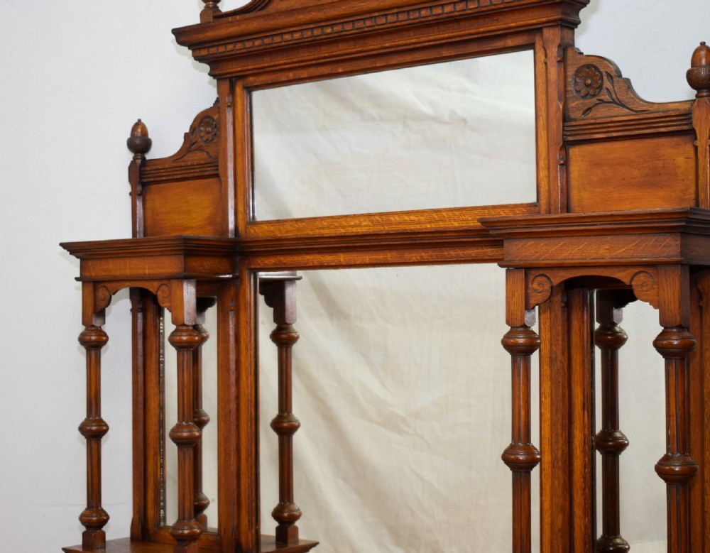 A Victorian carved oak overmantel mirror featuring turned side columns, small side display shelves, an arched pediment, and mirrored glass panels. View XV